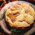 A whole ricotta cake with pears and sprigs of rosemary on a wooden board.