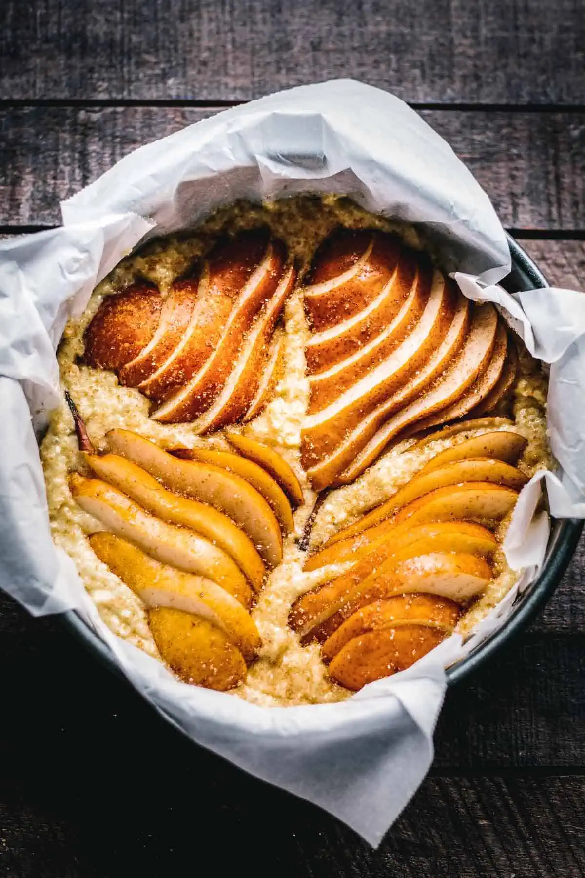 Sliced pears set into ricotta cake batter in a round pan.
