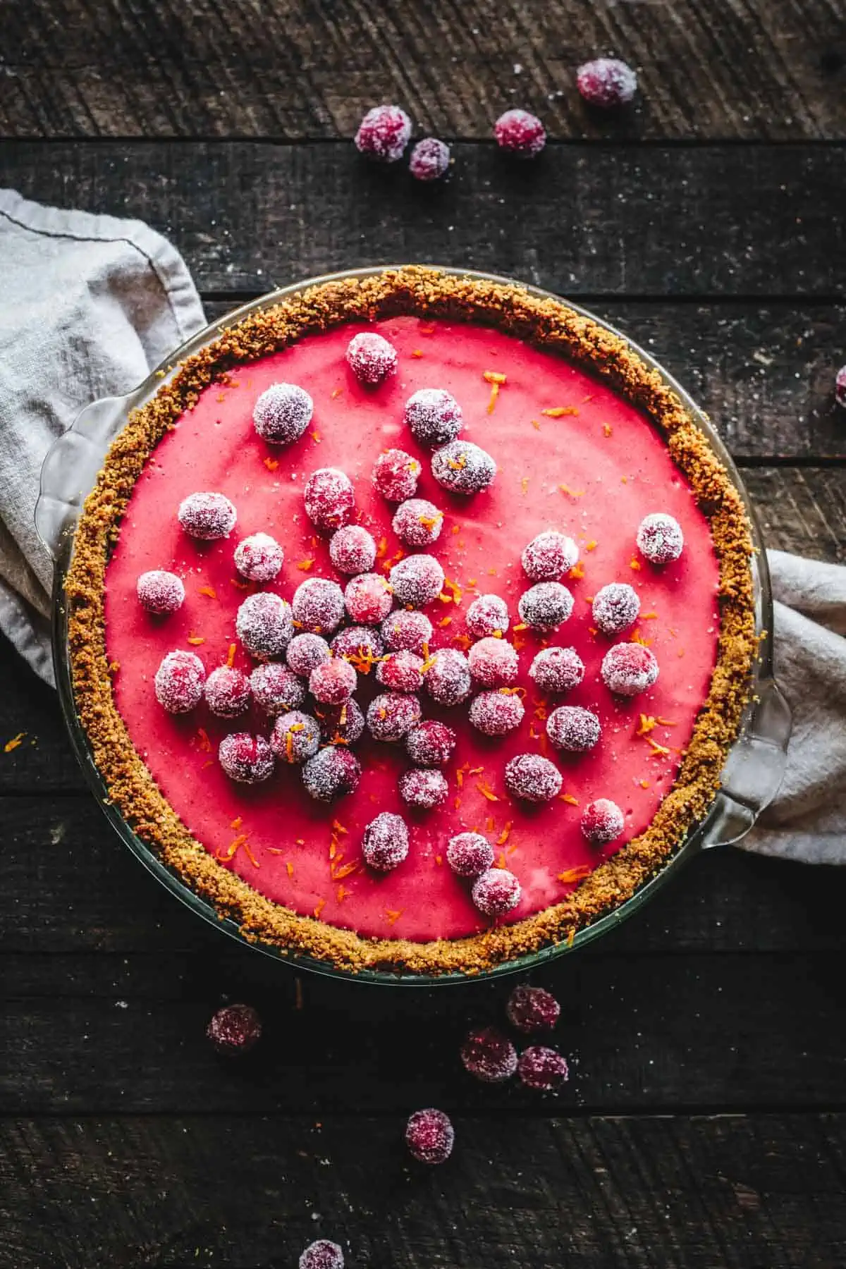 A bright pink Cranberry Pie with sugared cranberries on a dark background with linen napkin.