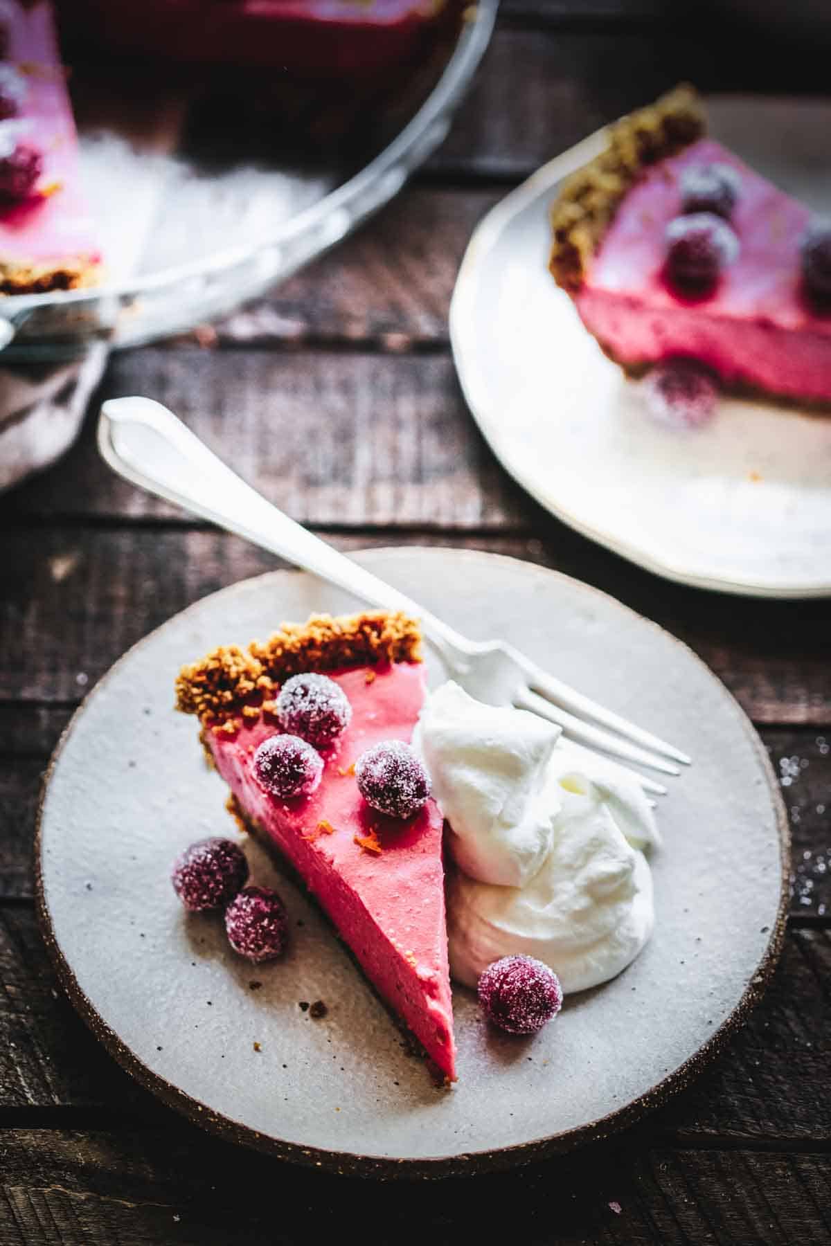 A slice of cranberry curd pie on a small plate with sparkling sugared cranberries and whipped cream.