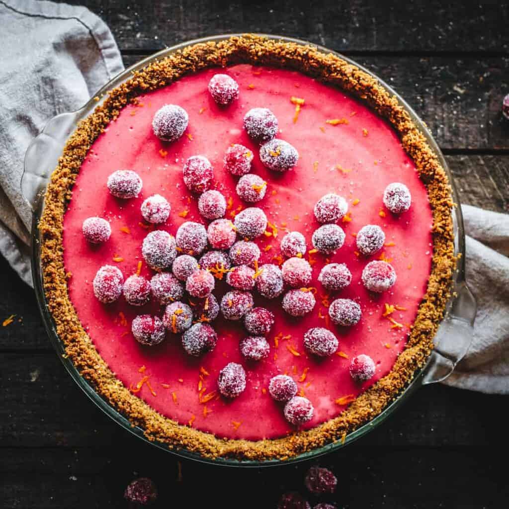 A whole creamy Cranberry curd Pie with sugared cranberries on a dark background.