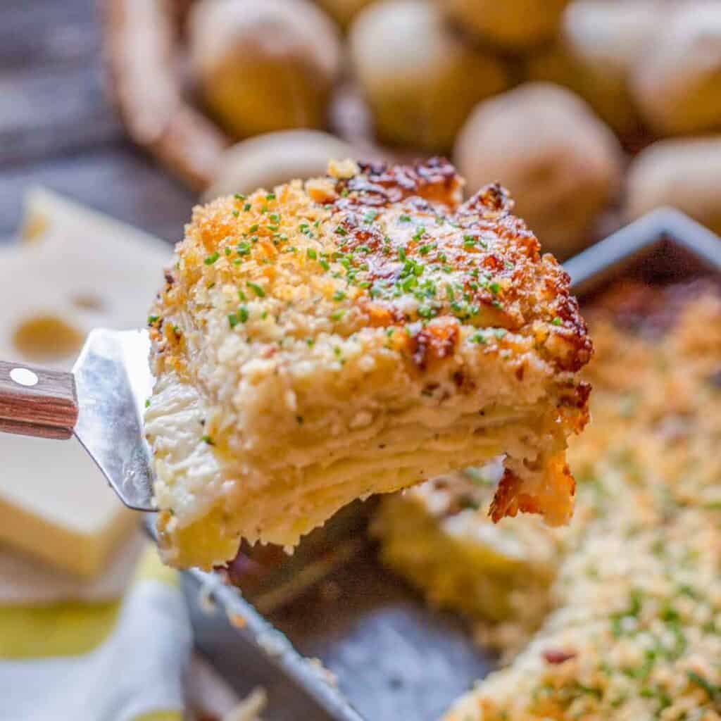 A spatula lifting a square of Dauphinoise potato gratin out of a pan.