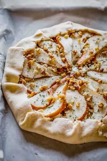 An unbaked pear galette on parchment paper, sprinkled with chopped walnuts.