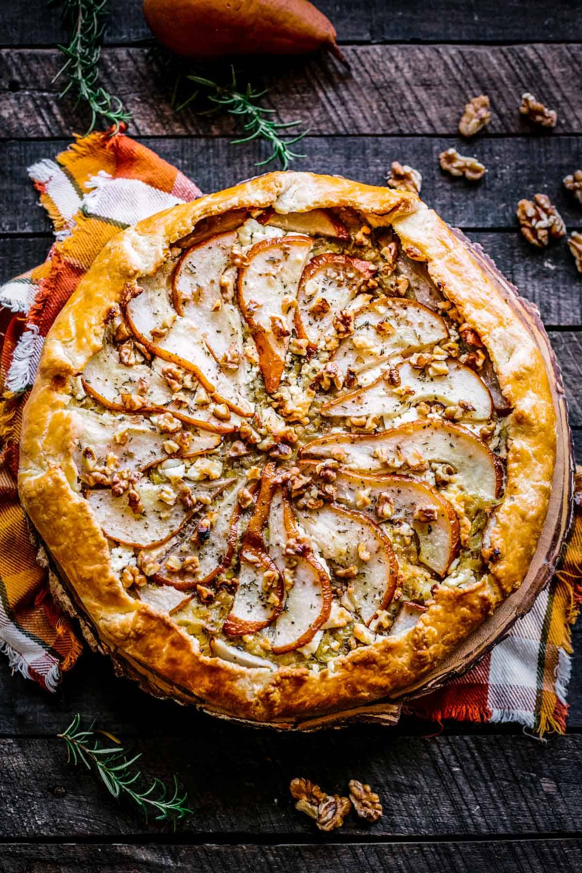 A pear galette with walnuts and goat cheese on an orange checkered napkin.