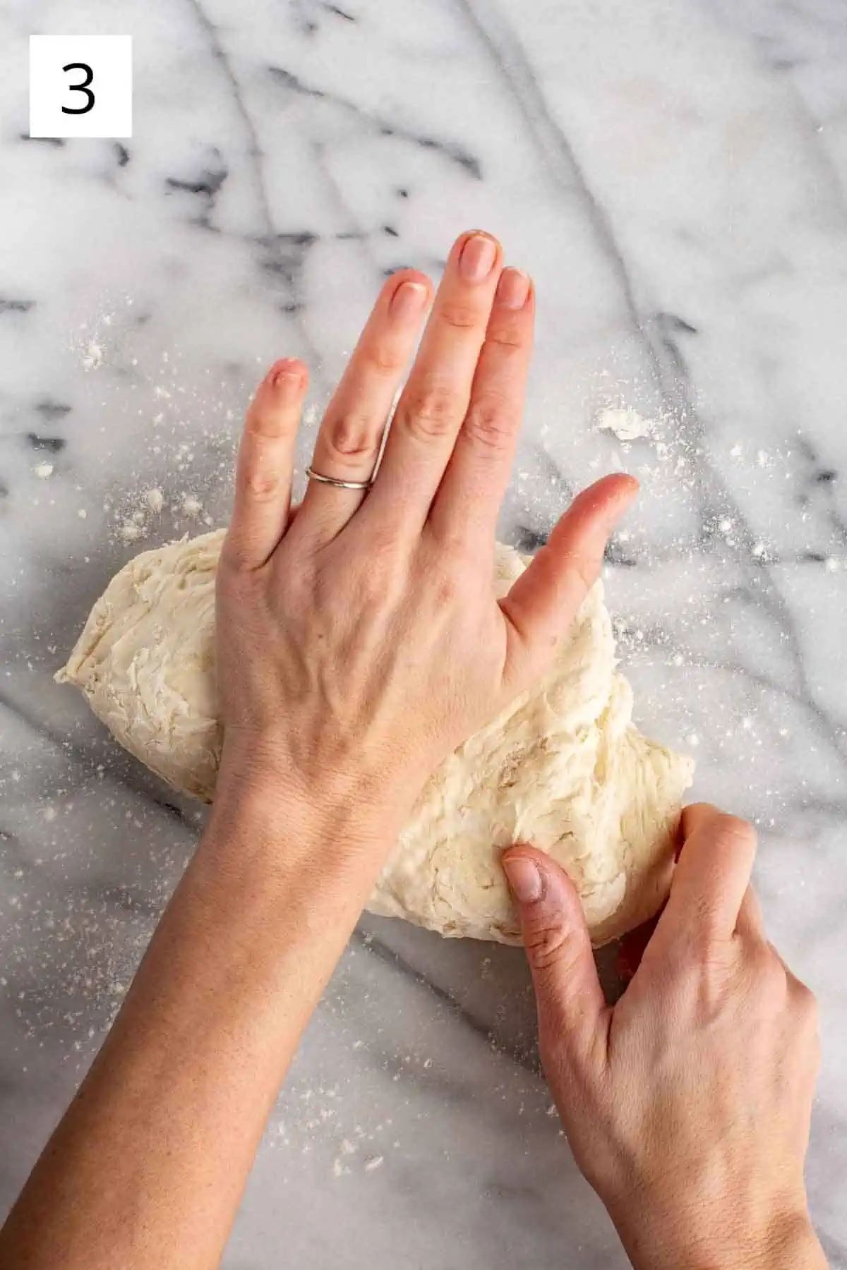 Hands kneading a large ball of pizza dough.