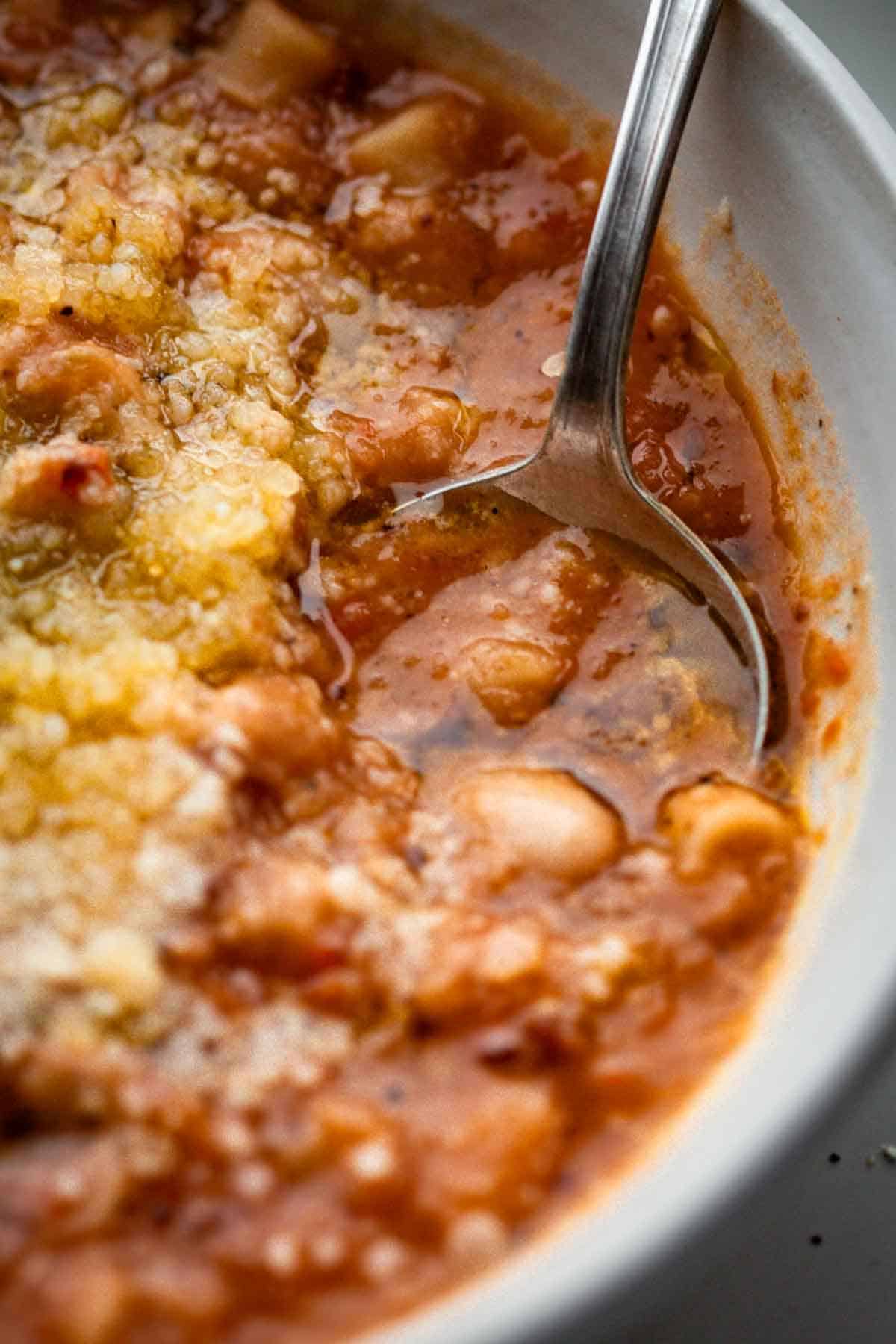 Close up of a spoon scooping up a spoonful of pasta e fagioli.