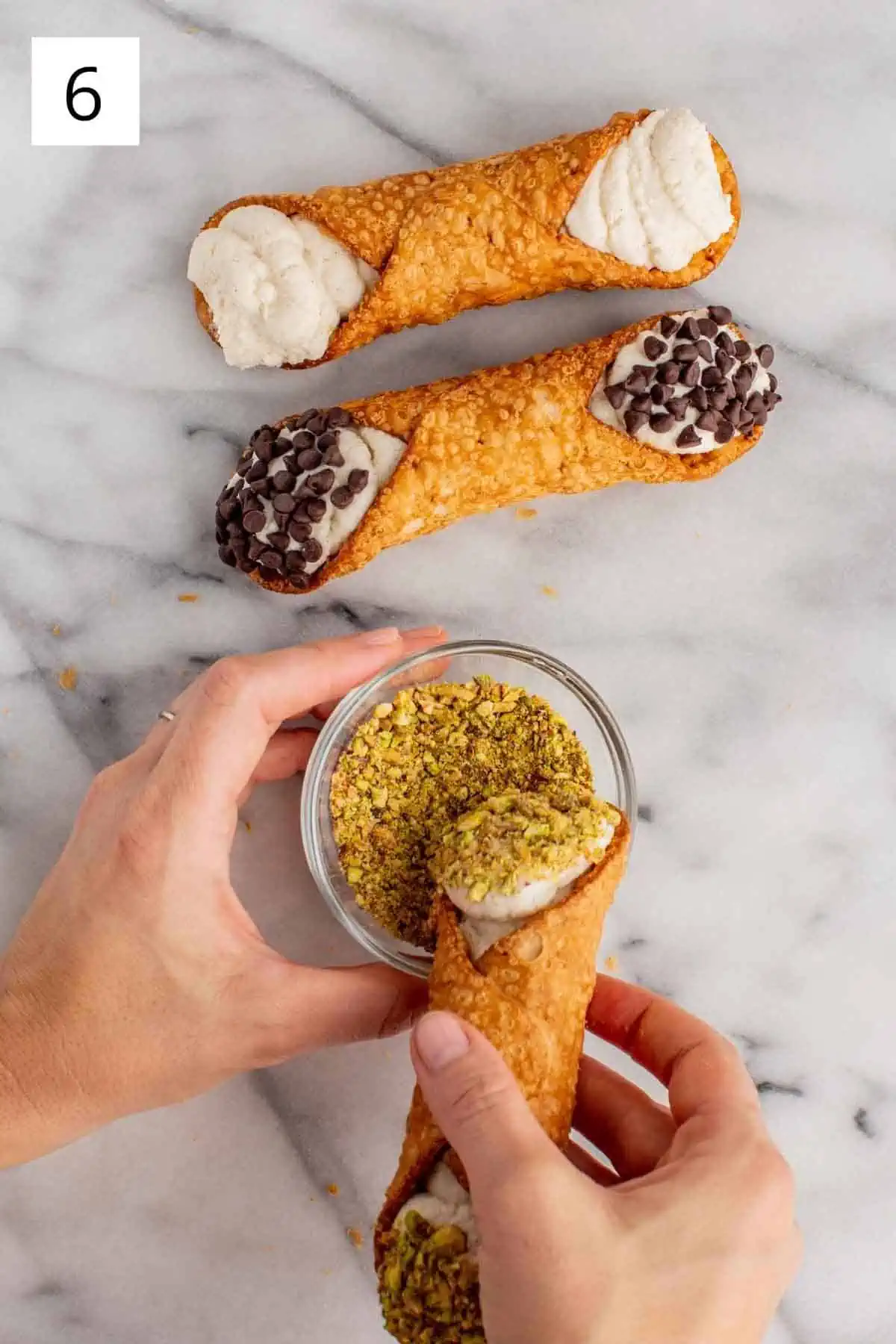 Dipping a cannoli into crushed pistachios.