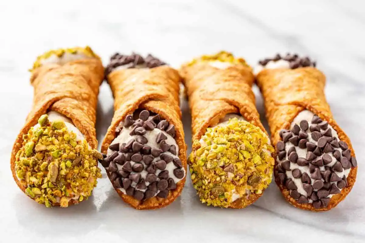 Close up of cannoli stuffed with ricotta filling and garnished with chocolate chips and pistachios.