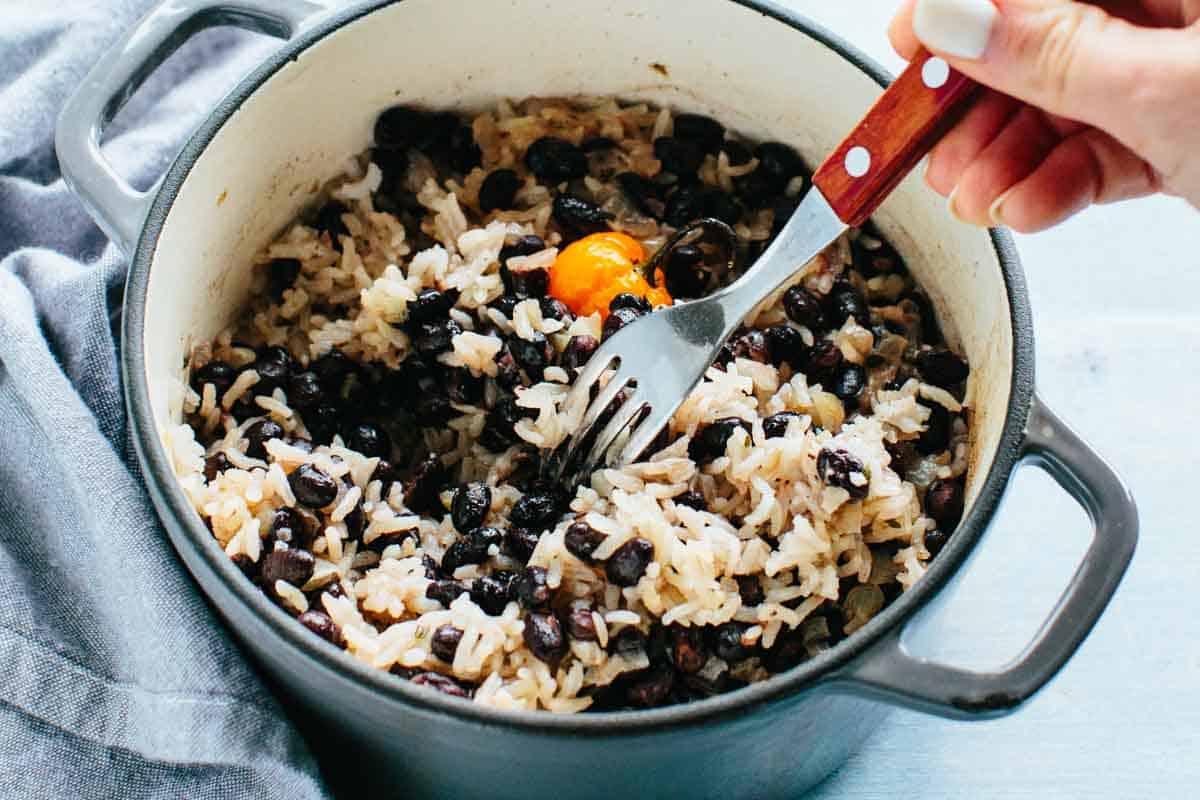 A fork flaking a pot of coconut rice and beans.