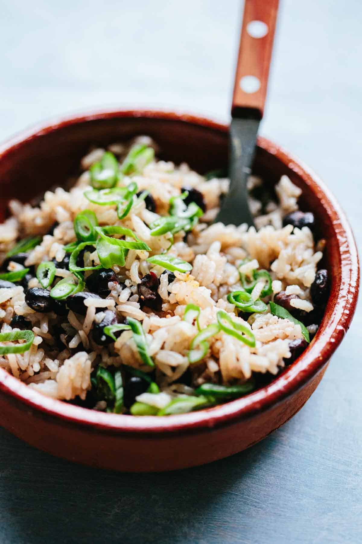 A bowl of coconut rice and beans with a fork and scallions on top.