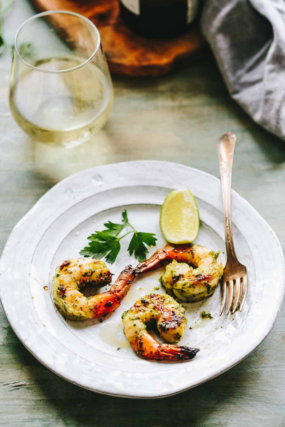 A gray plate with three grilled shrimp and a glass of white wine.
