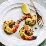 Three marinated grilled shrimp with a lime and a fork.