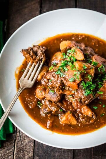 Awhite bowl of Irish stew with a fork.