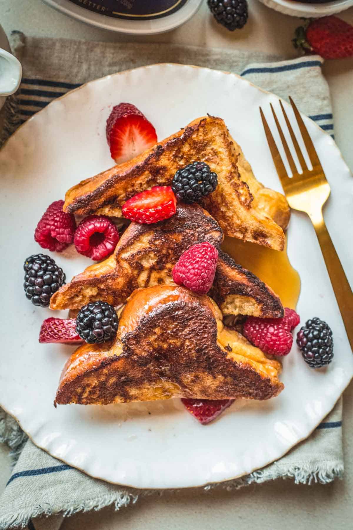 Three triangles of French toast on a plate with maple syrup and berries.