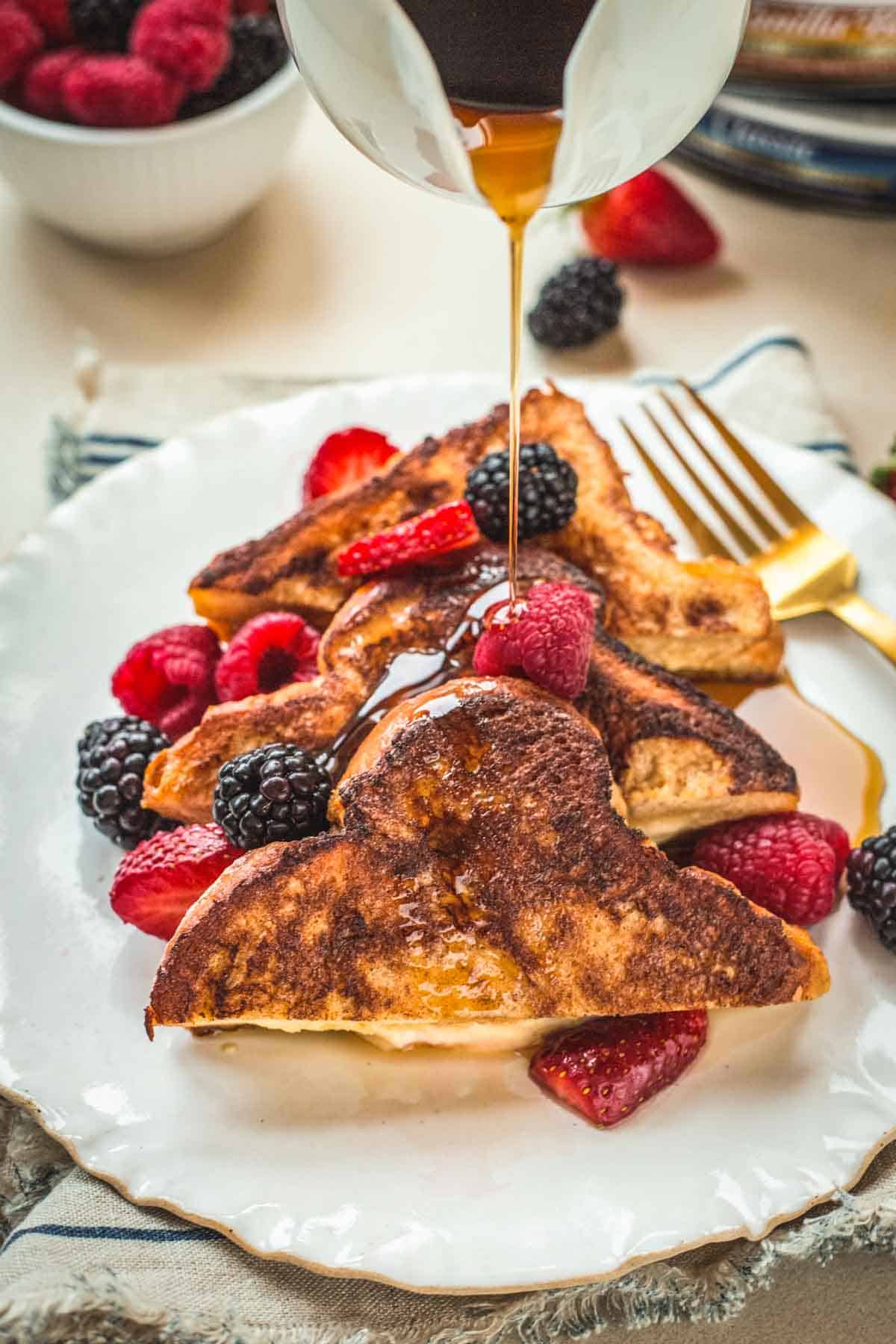 Maple syrup being drizzled on a plate of stuffed French toast.