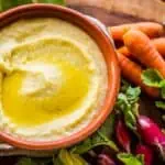 A bowl of Greek garlic and potato dip with carrots and radishes.