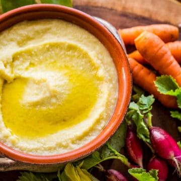 A bowl of Greek garlic and potato dip with carrots and radishes.