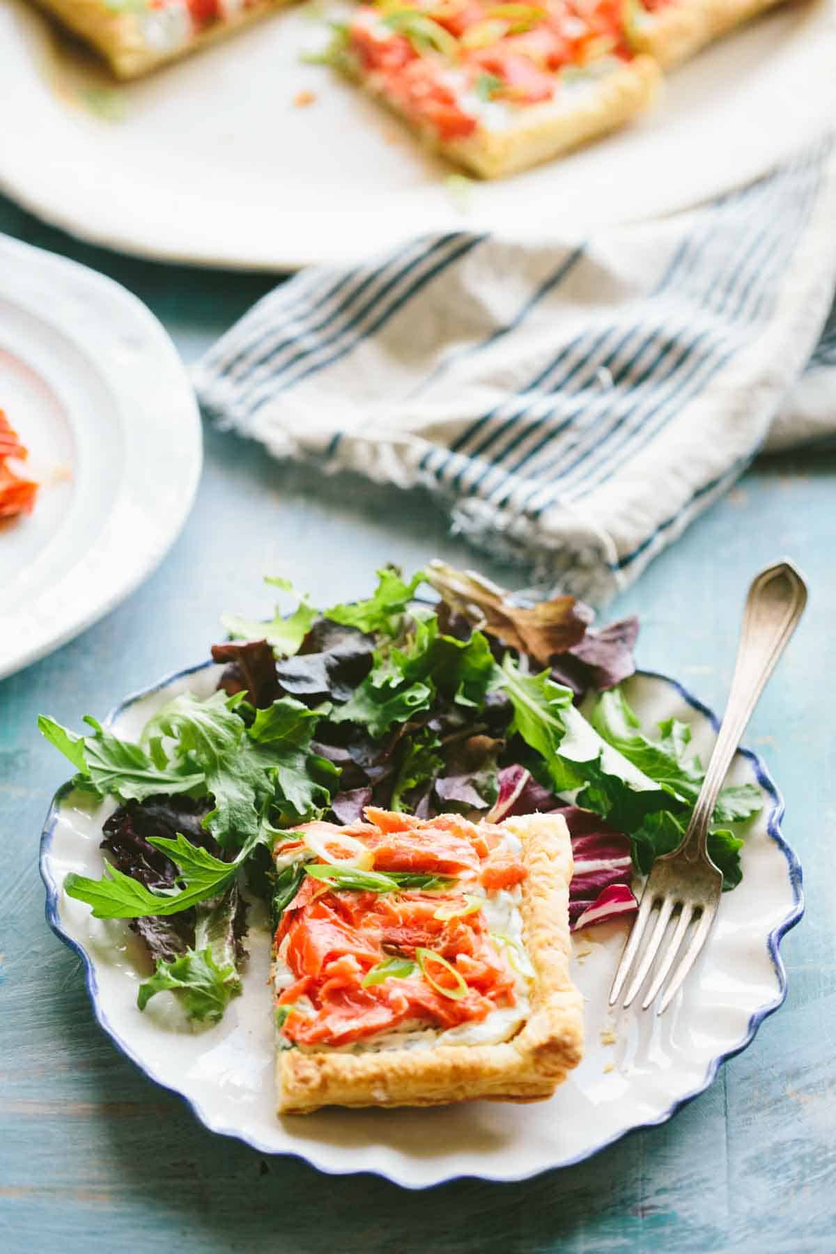 A plate with a green salad and piece of salmon tart.