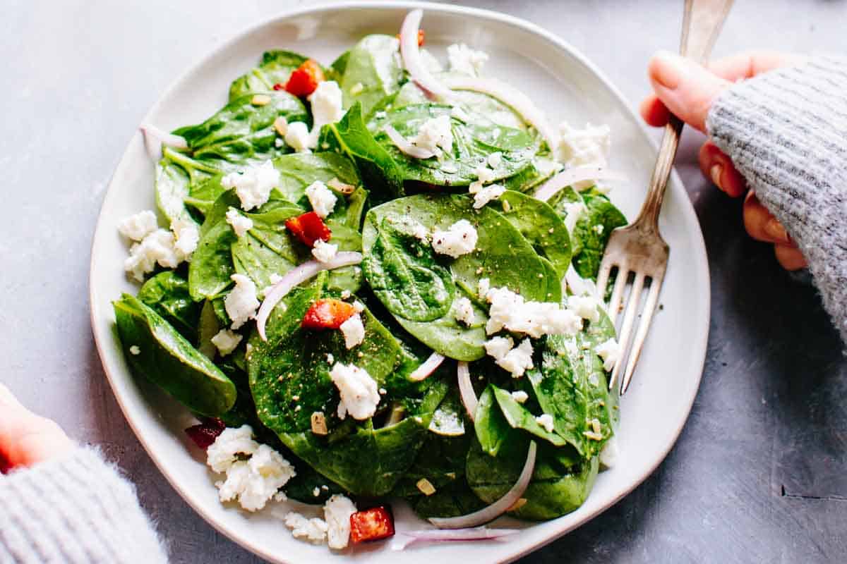 A fork grabbing a bite of warm spinach salad with pancetta.