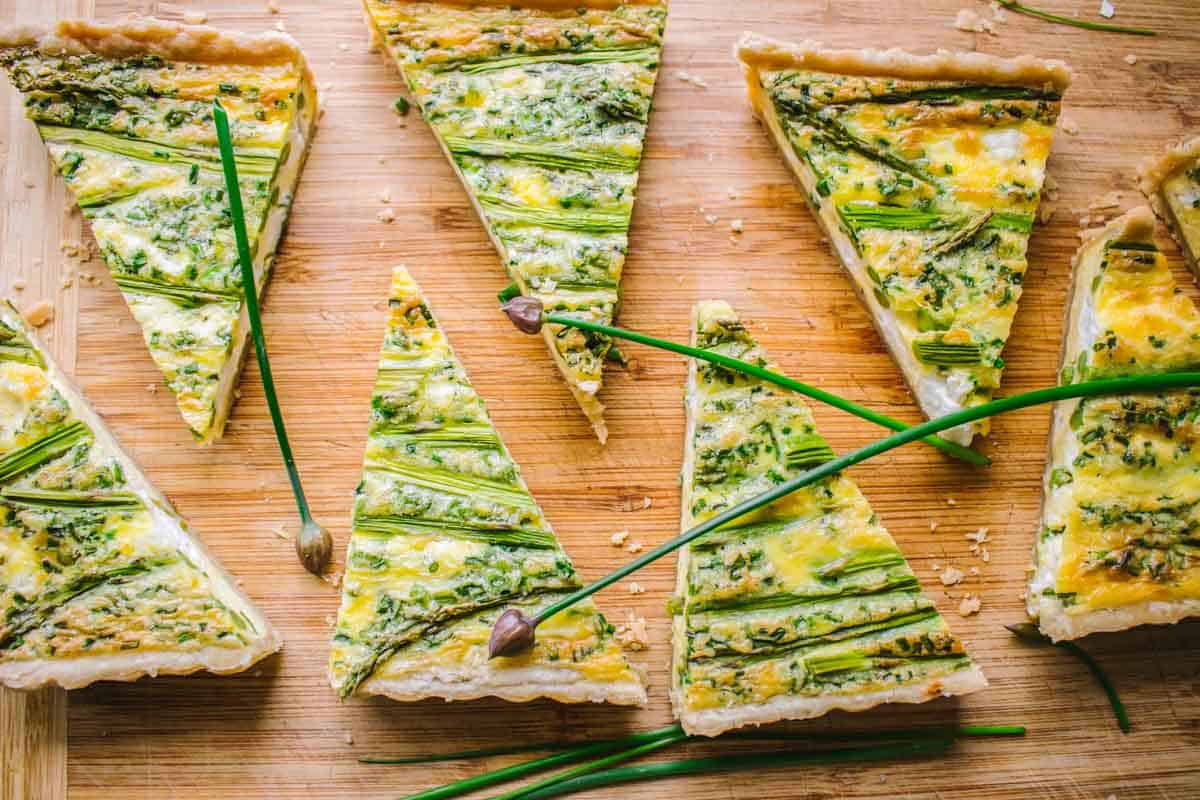 Slices of asparagus and goat cheese quiche on a plate with chive blossoms.