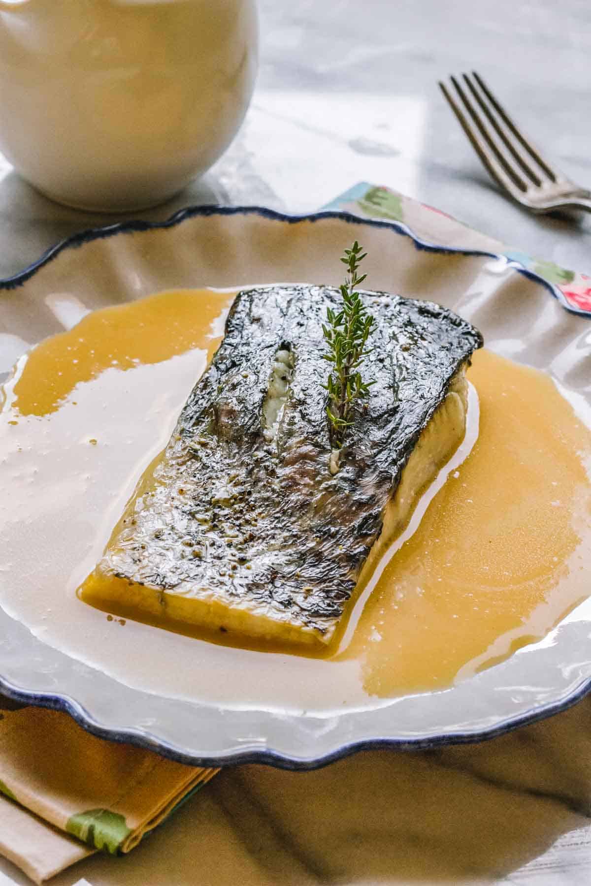 A piece of skin-on fish perched on top of sauce beurre blanc.