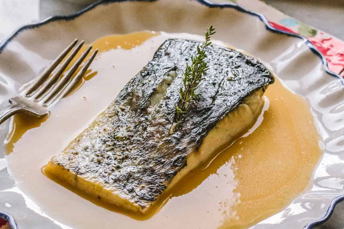 A pool of French butter sauce with a piece of fish on top.