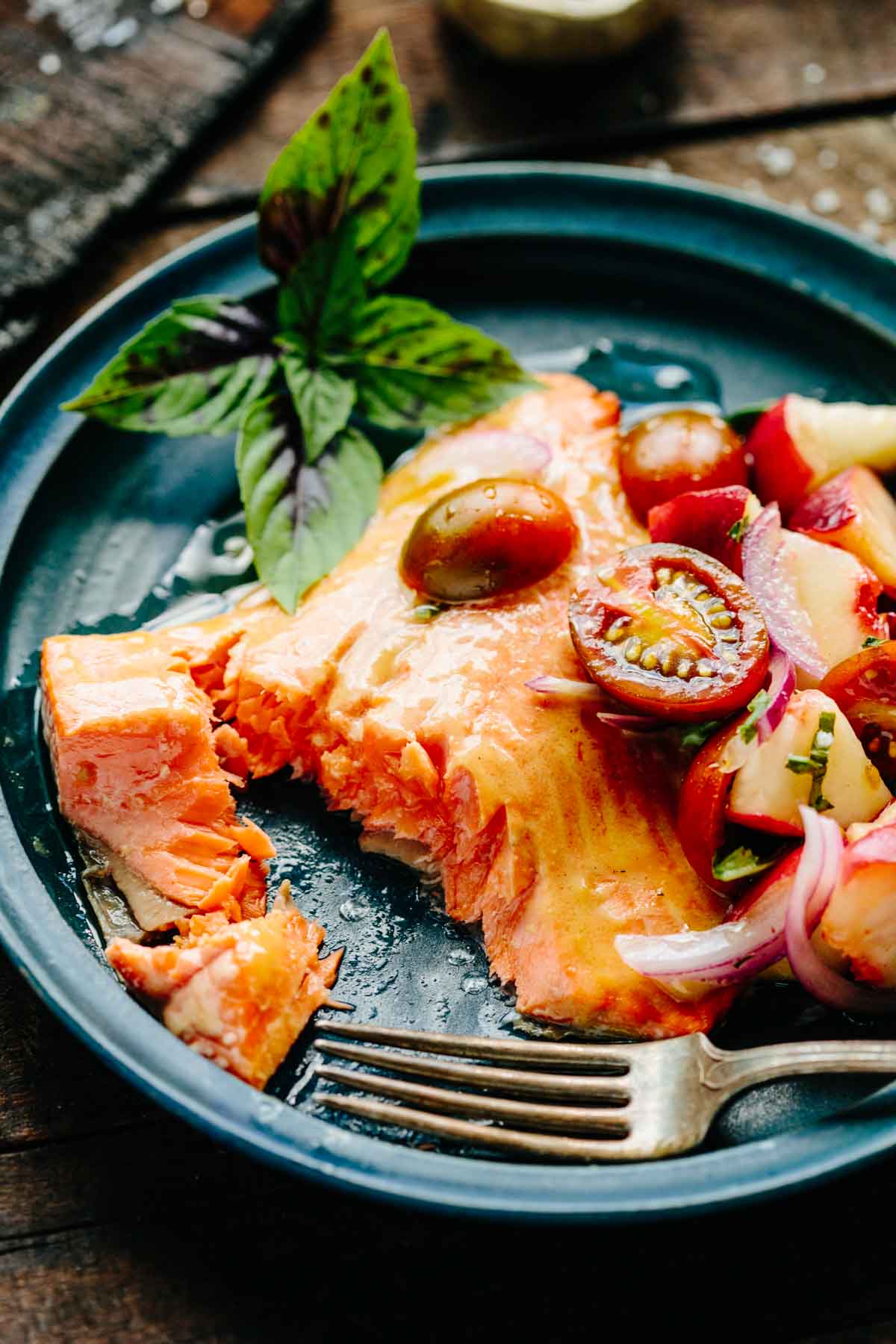 Roasted salmon on a plate with tomatoes and a bite taken out of it.