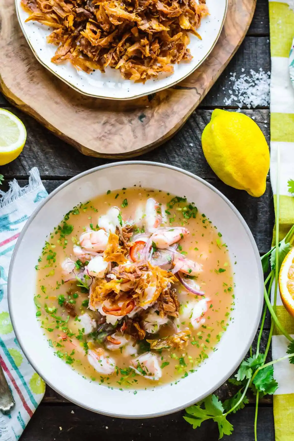 A bowl of Ecuadorian shrimp ceviche with fried plantains and lemons on the side.