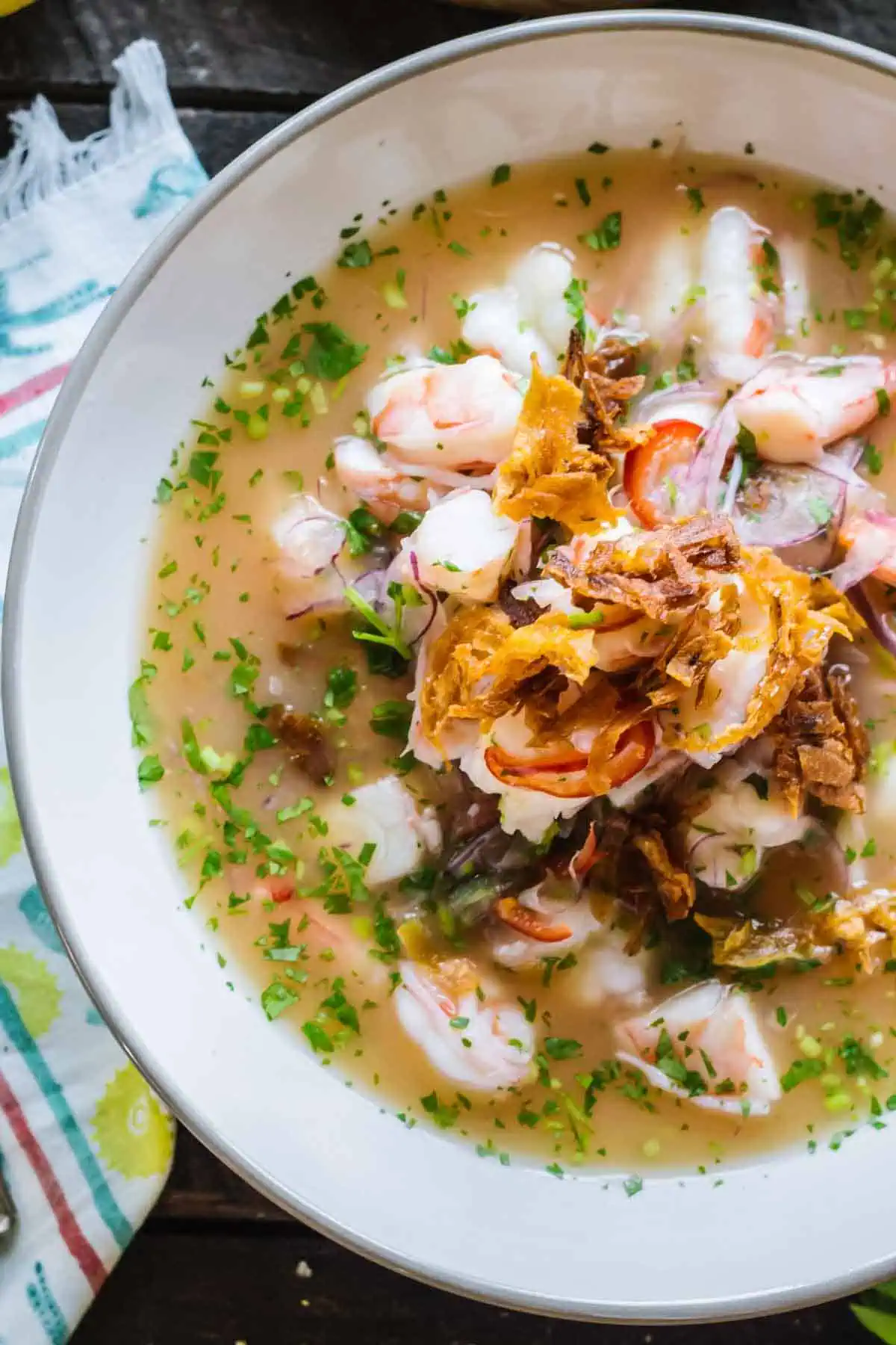 A white bowl filled with shrimp ceviche and fried plantains.