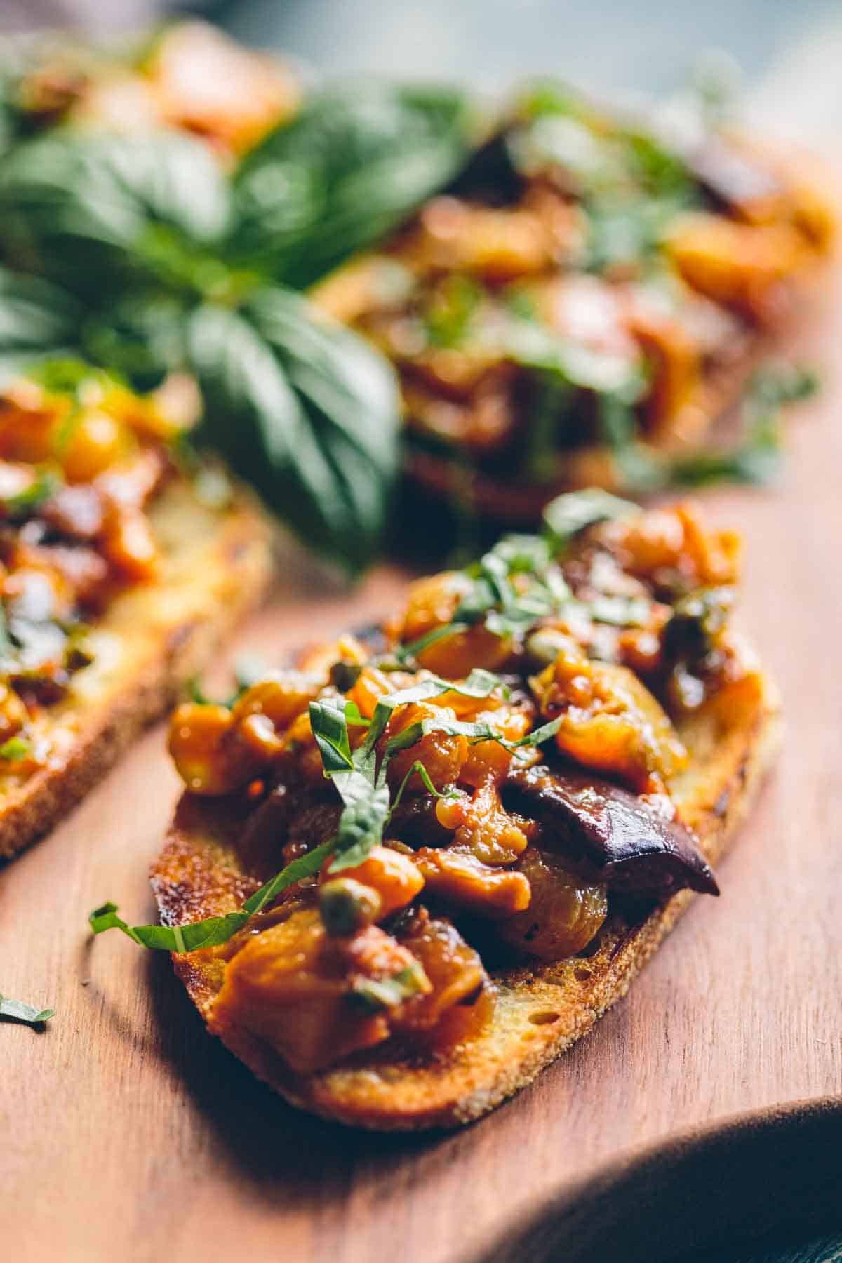 A tray of crostini with eggplant caponata on top and a sprig of basil.