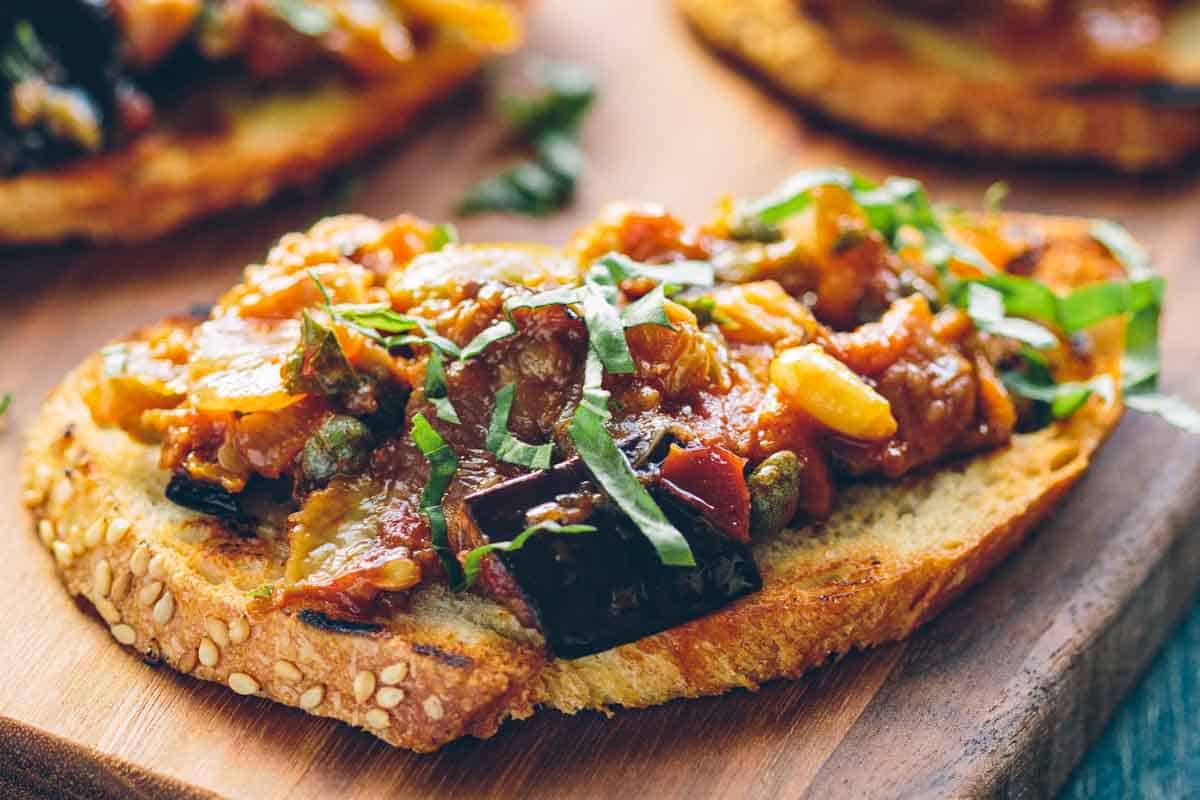 A piece of crostini topped with Sicilian caponata with pine nuts and raisins.