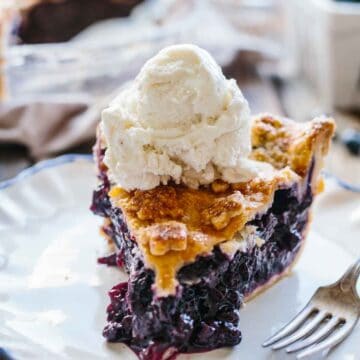 A slice of old fashioned blueberry pie with vanilla ice cream on top.