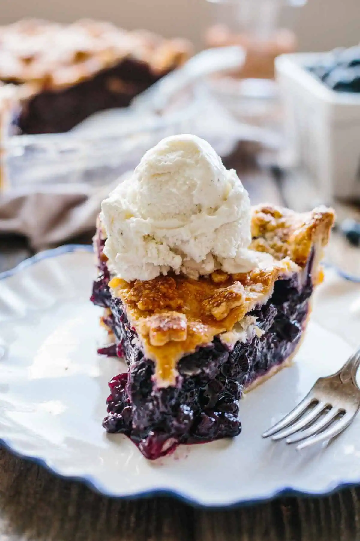 A slice of old fashioned blueberry pie with vanilla ice cream on top.