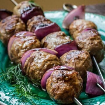Lamb meatballs and red onion slices on metal skewers on a green plate.