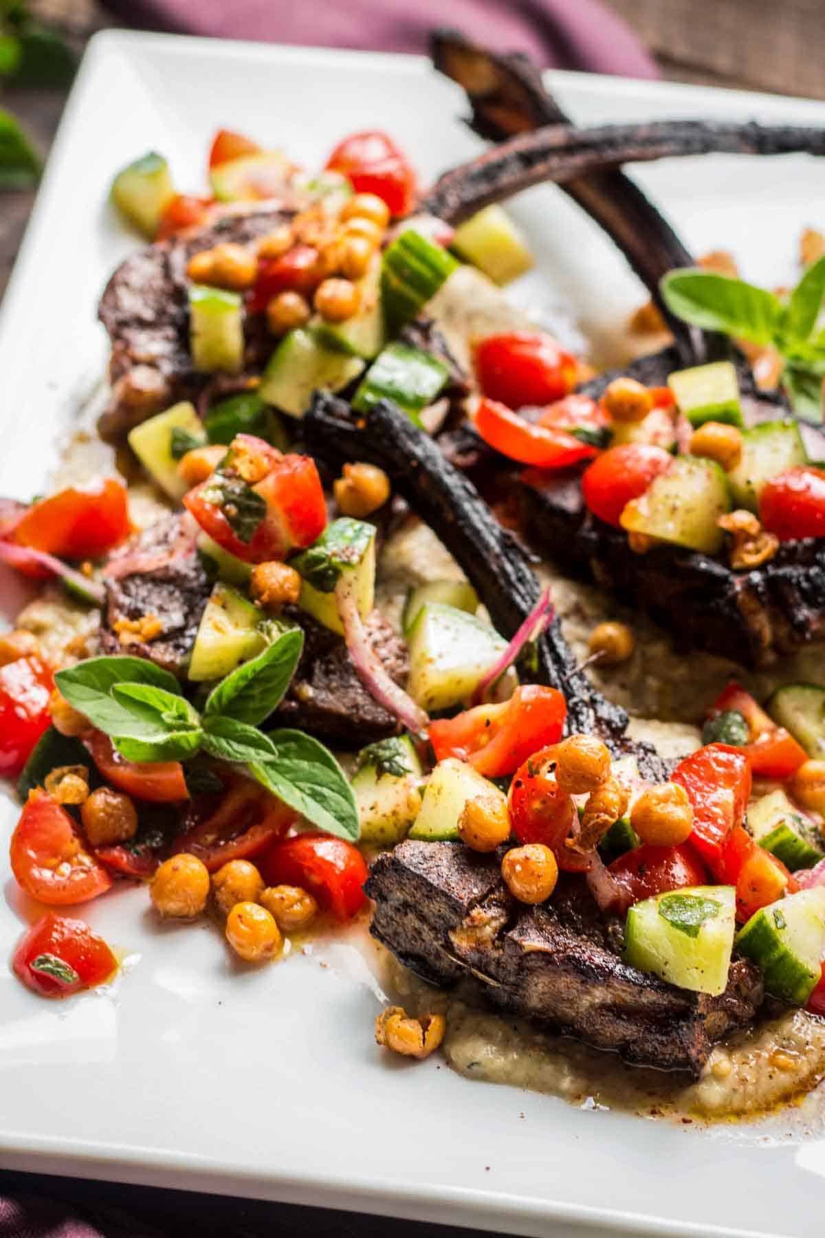 Lamb chops and chickpea tomato cucumber salad on a white serving platter.