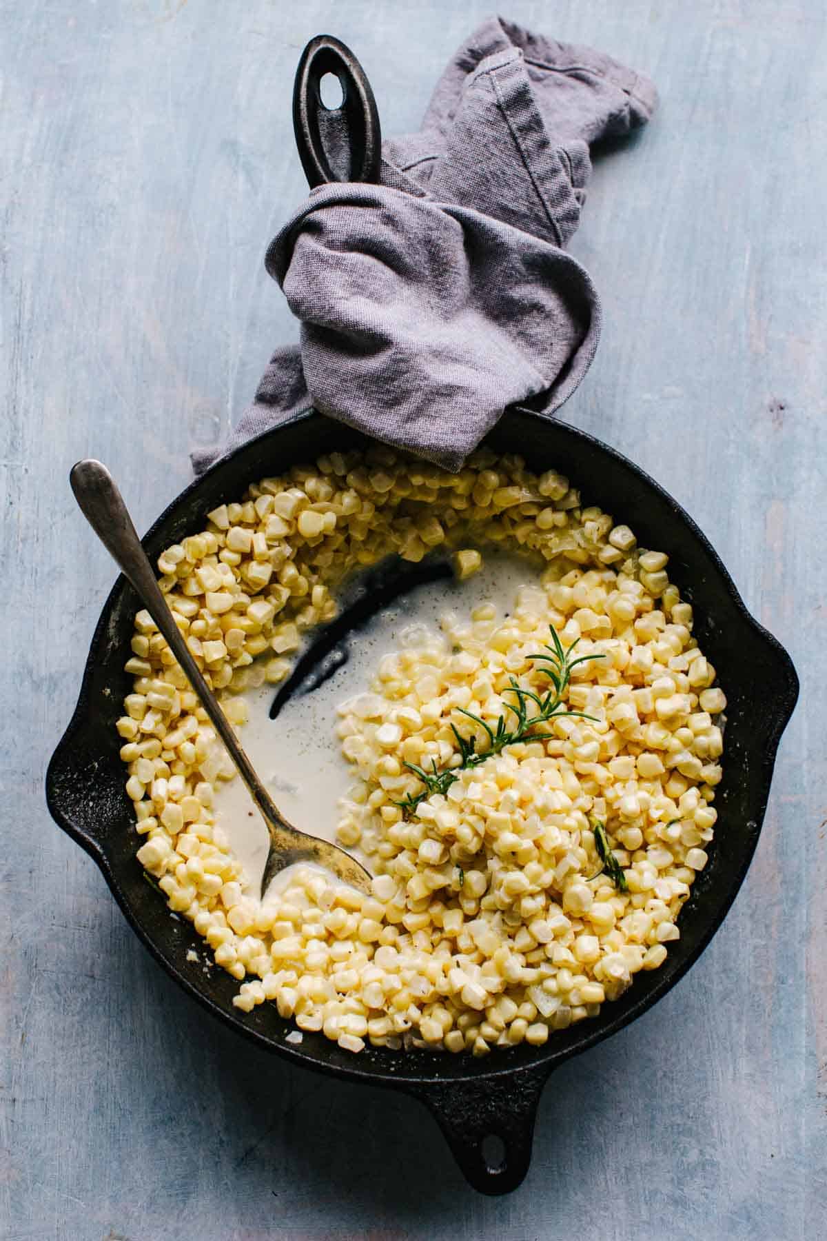 Homemade creamed corn in a cast iron skillet with a spoon.