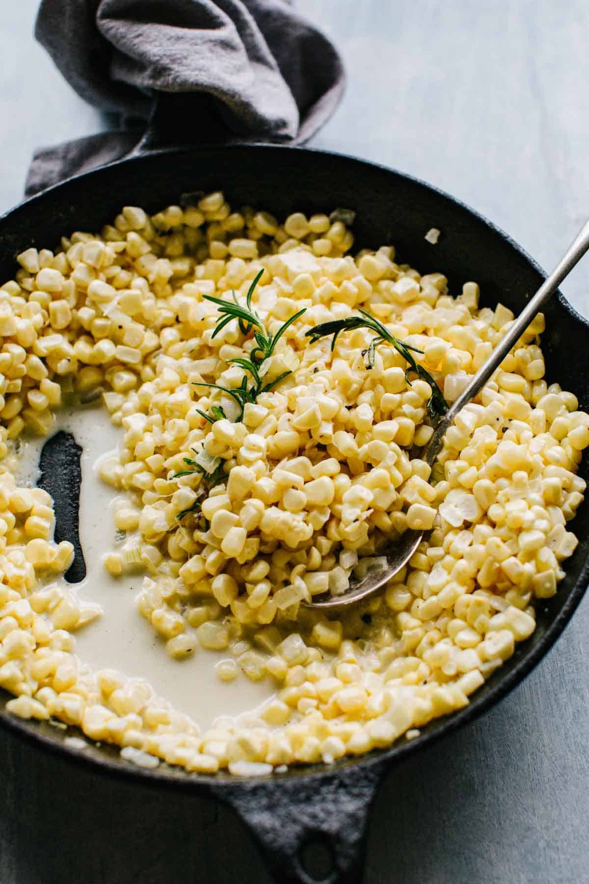 A spoon scooping homemade creamed corn from a pan.