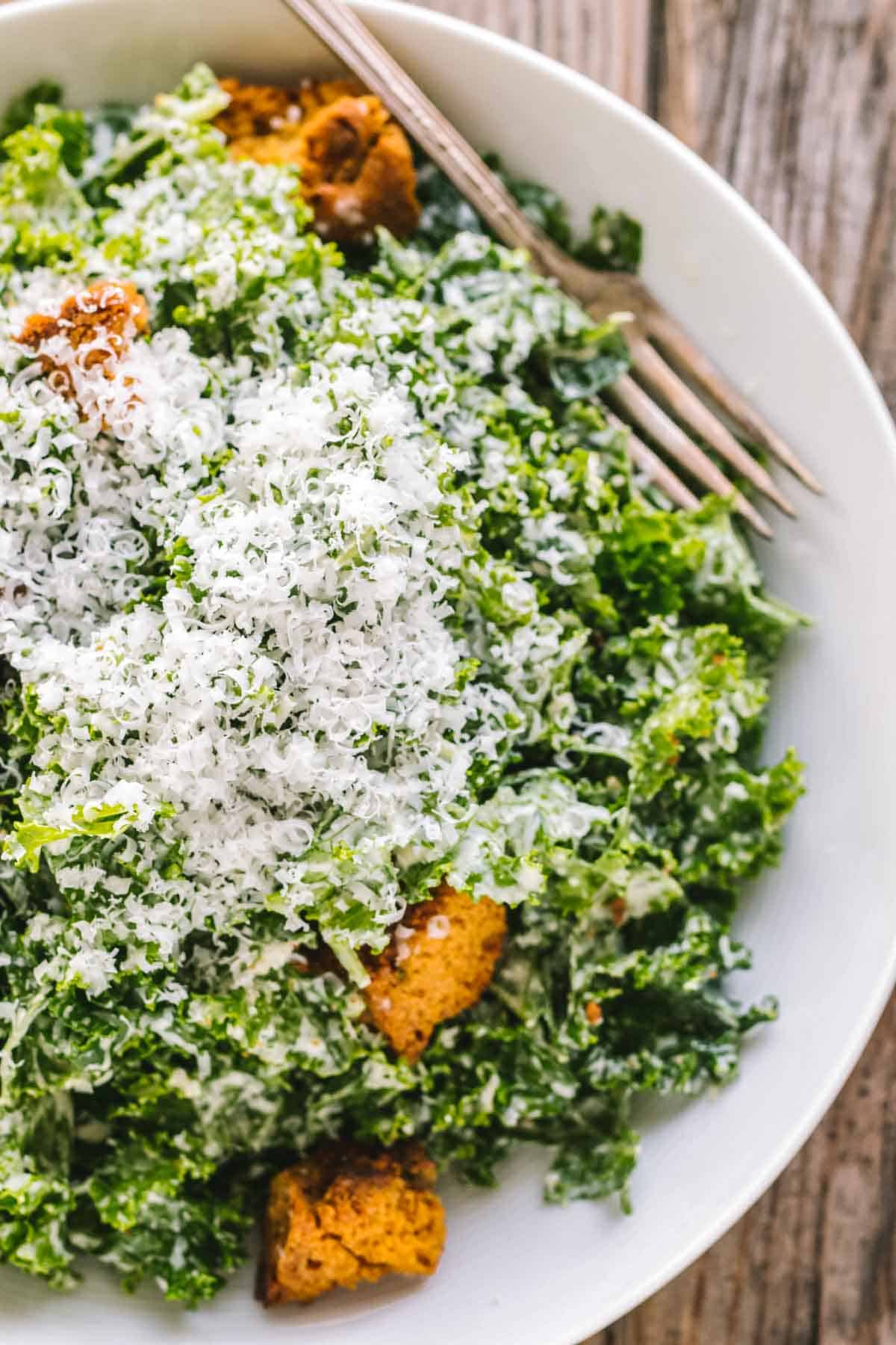 Kale Caesar salad with croutons, parmesan cheese and a fork.