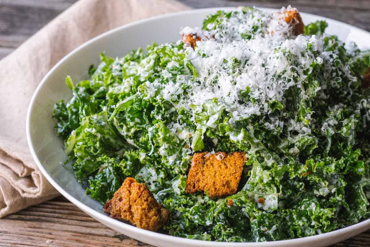 A bowl of kale salad with big croutons and parmesan cheese on top.