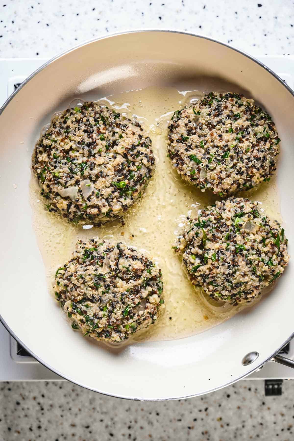 Kale and quinoa cakes frying in a pan.