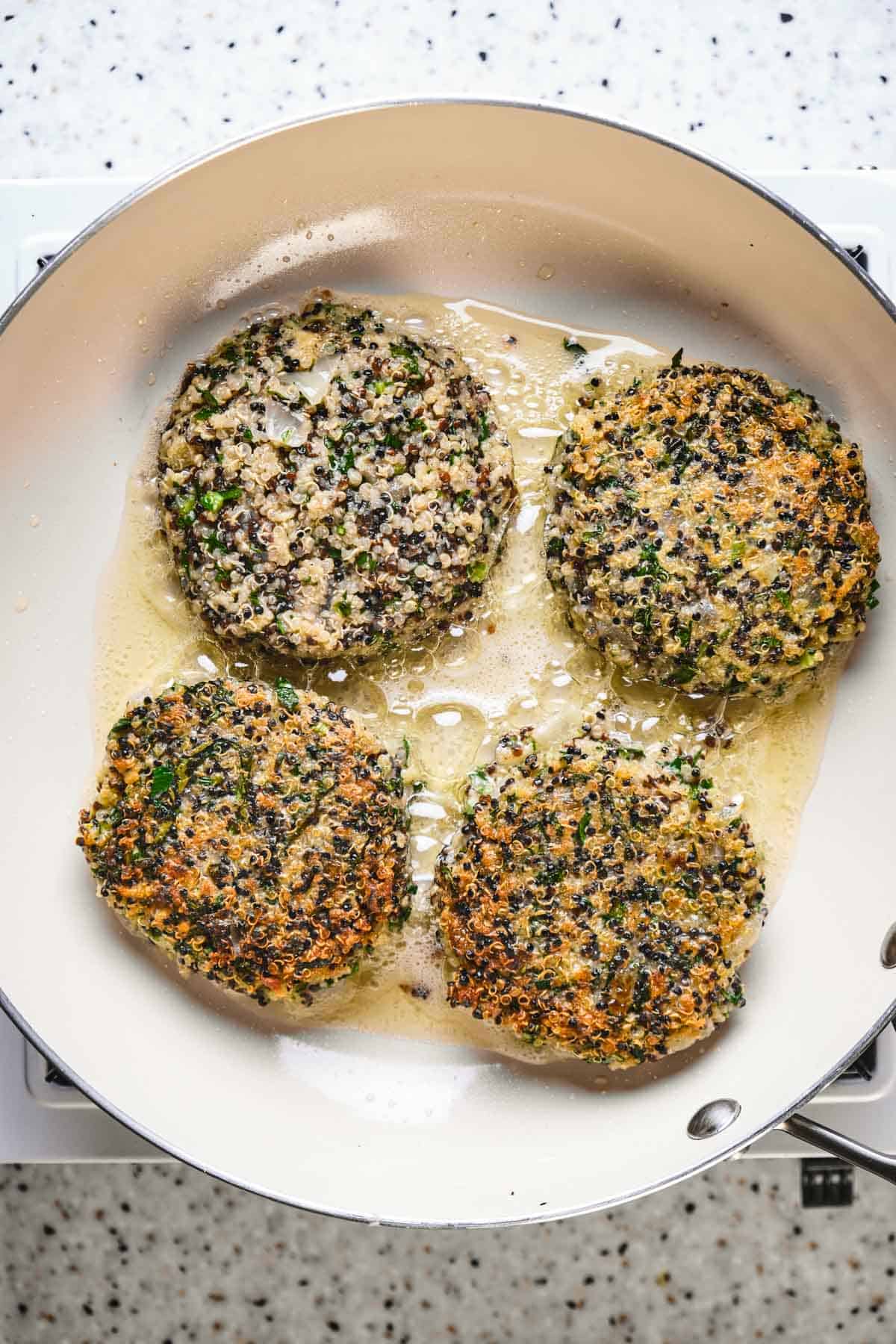 Kale and quinoa cakes crisped and browned in a frying pan.