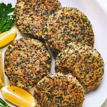 Kale and quinoa cakes on a white plate with lemon wedges.