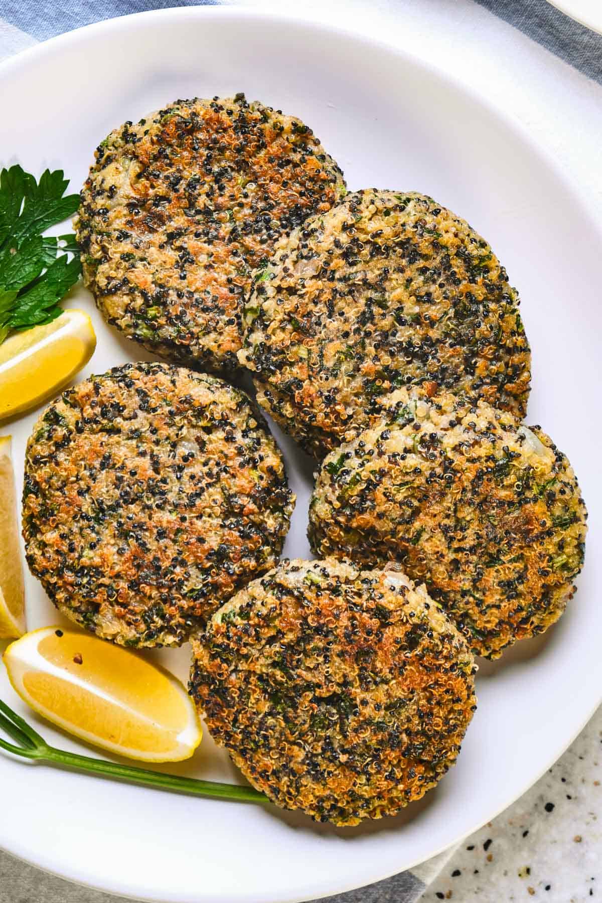 Kale and quinoa cakes on a white plate with lemon wedges.