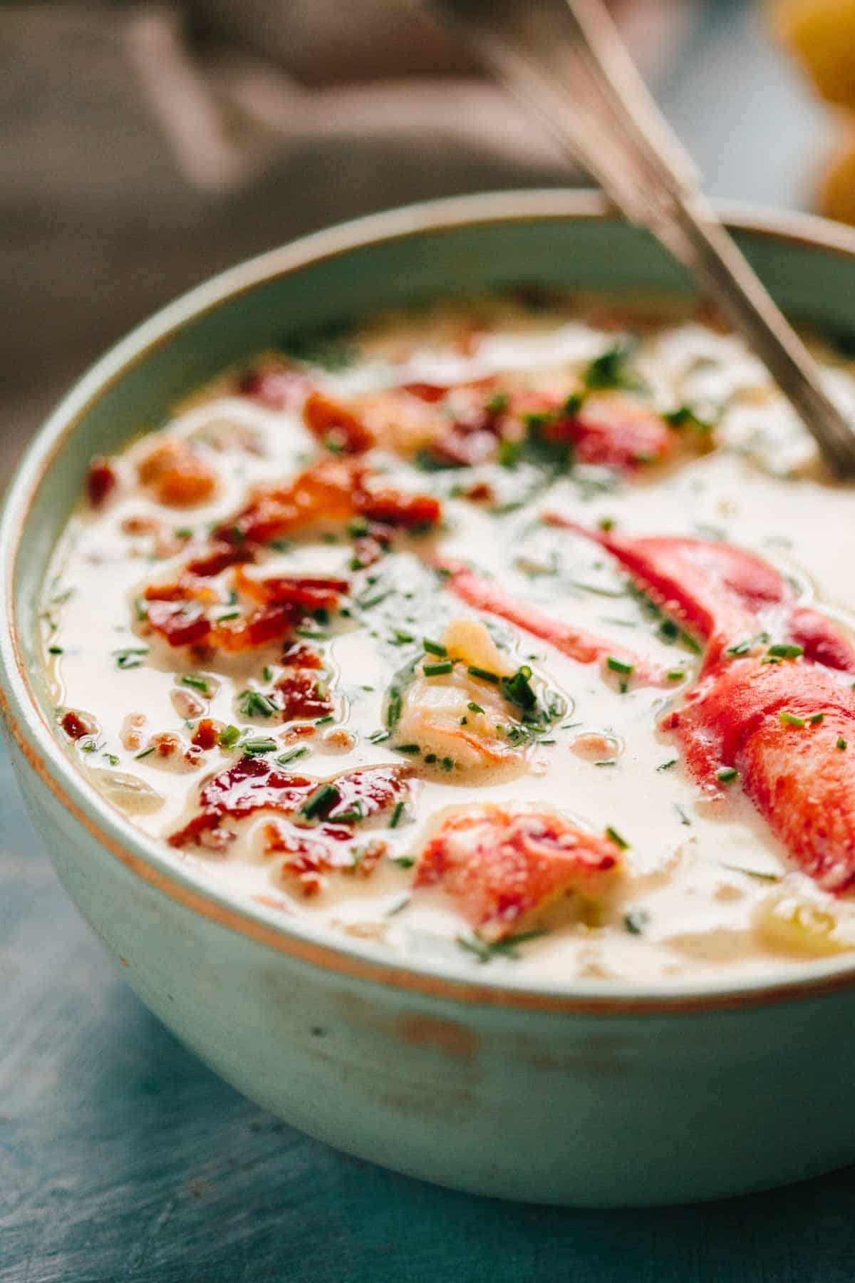 A pale green bowl of lobster chowder with a piece lobster claw meat.
