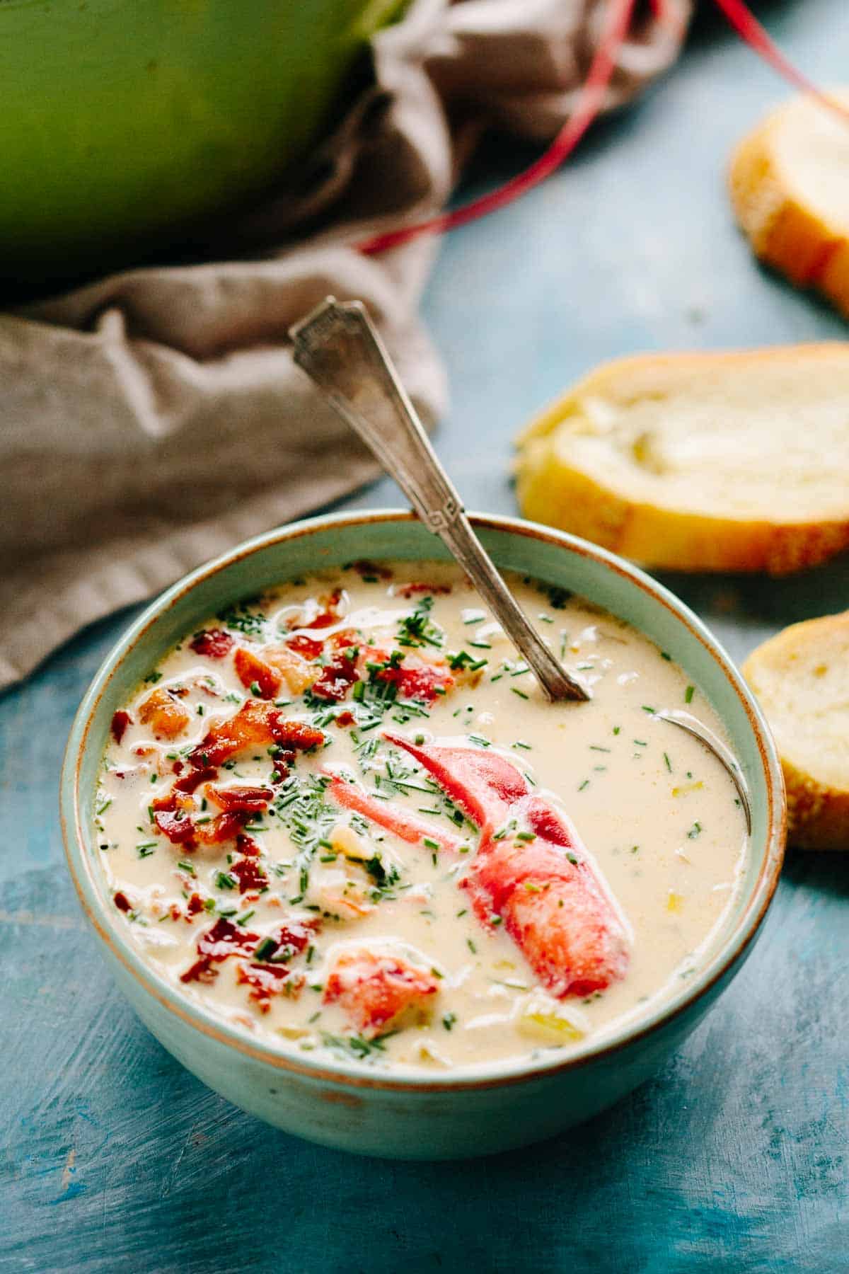 A bowl of lobster corn chowder with a spoon in it.