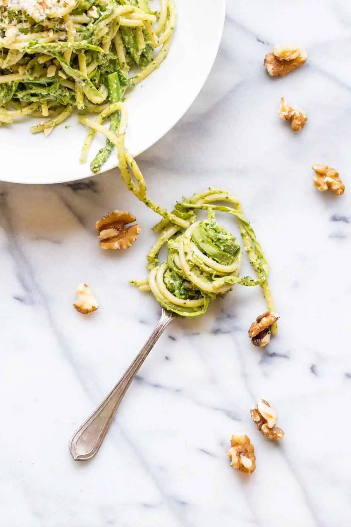 A bowl of green pesto pasta and a fork with pasta twirled around it.