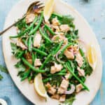 A large platter of Italian tuna salad with green beans, parsley and lemon with a serving fork.