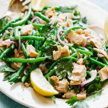 A platter of Italian tuna and green bean salad with lemon wedges.