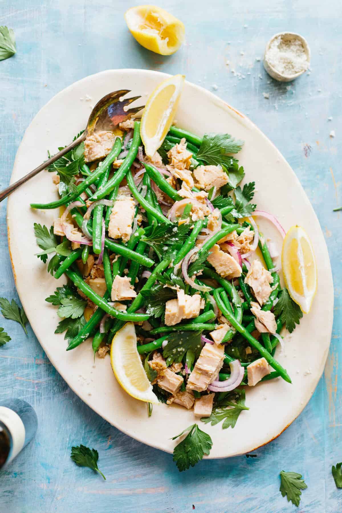 A large platter of Italian tuna salad with green beans, parsley and lemon with a serving fork.