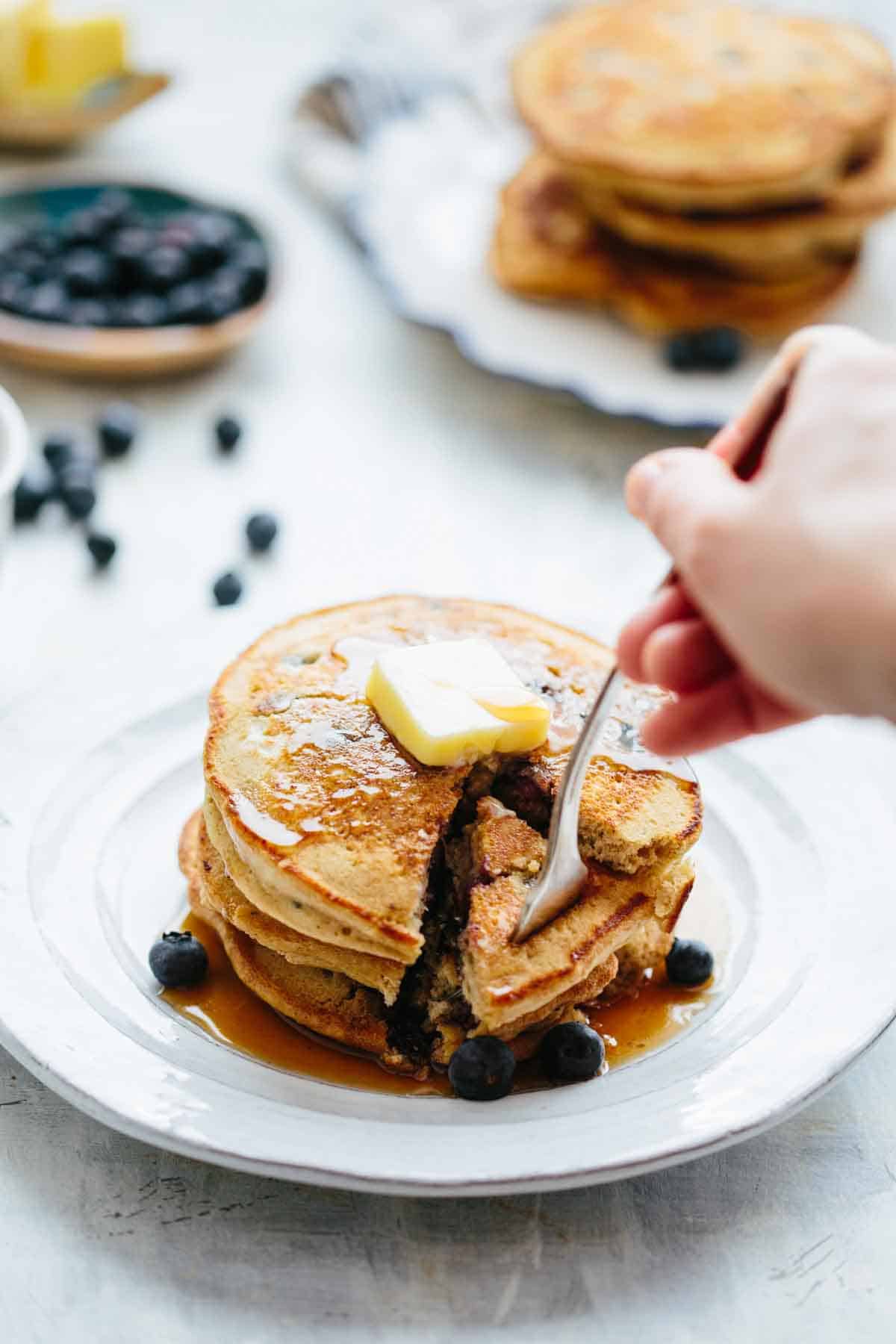 A fork digging into a piece cut out from a stack of pancakes.